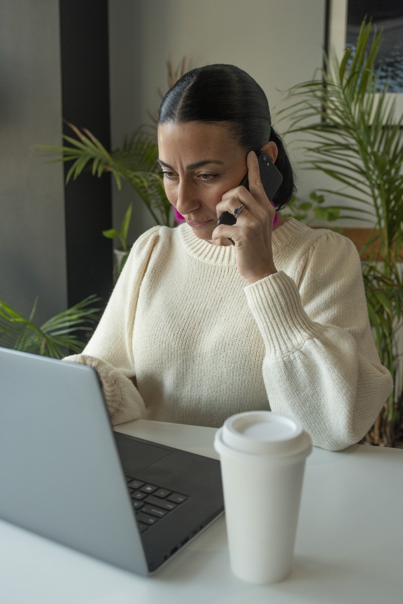 A woman on a phone call, also looking at her laptop